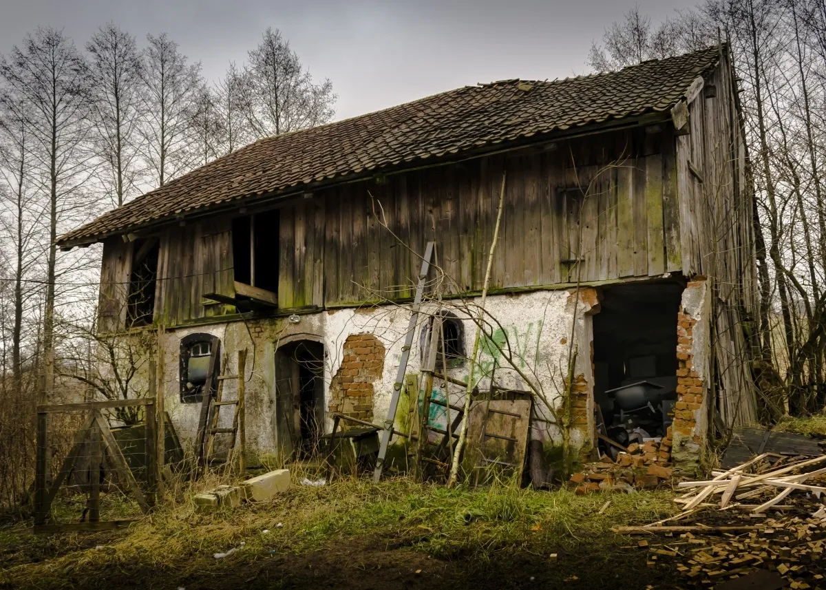 Weathered rural building with leaning doors and broken windows